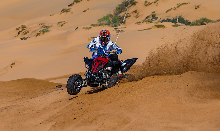 Guest riding Yamaha sports quad over red dunes